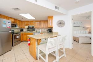 una cocina con armarios de madera y una isla de cocina con sillas blancas. en Phoenix VII 7503 condo, en Orange Beach