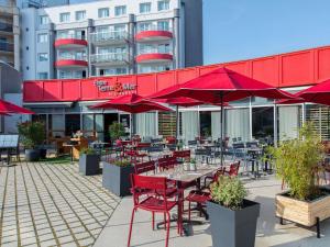 un patio avec des tables et des chaises et des parasols rouges dans l'établissement ibis La Baule Pornichet Plage, à Pornichet