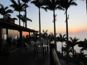 una terraza con sillas y palmeras al atardecer en Pousada Singuitta - Ilhabela en Ilhabela