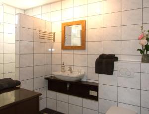 a white tiled bathroom with a sink and a mirror at B&B Duinroos De Koog - Texel in De Koog