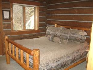 a bed in a log cabin with a window at Relaxing Glamping Vacation: Fantastic Log Cabin with a Hot Tub in Darby, MT in Peaks and Pines Park