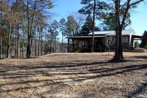 a house with a tree in front of a dirt yard at Secluded Cabin by the Black Fork River near Ouachita National Forest, Oklahoma in Hodgen