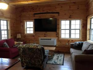a living room with a flat screen tv in a log cabin at Authentic Stunning Cabin Rental with Private Jacuzzi near Huntington, West Virginia in Genoa