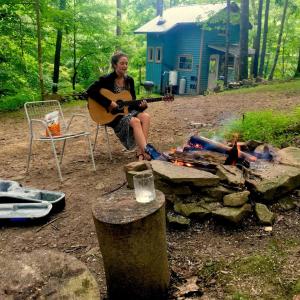 Una mujer tocando una guitarra junto a un fuego en Rustic Off-Grid Cabin Getaway near Wayne National Forest, Ohio, en Athens