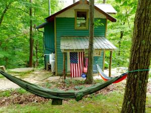 Una hamaca frente a una casa con una bandera estadounidense. en Rustic Off-Grid Cabin Getaway near Wayne National Forest, Ohio, en Athens