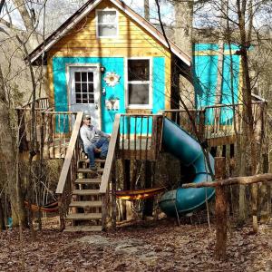 a man sitting on a slide in front of a house at Enchanting Tree House with a Slide on 200 Acres for a Family Adventure in Germantown, Kentucky in Germantown
