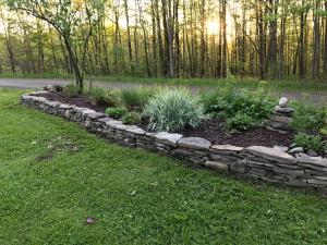 a stone retaining garden with plants in a yard at Pristine and Cozy Cabin Rental Overlooking Pond near Rochester, New York in Naples