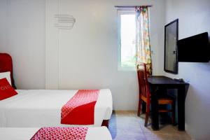 a bedroom with two beds and a desk and a window at OYO 94787 Hotel Mulana in Banda Aceh