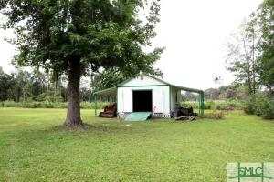 einen kleinen weißen Schuppen mit einem Baum auf einem Feld in der Unterkunft Quaint Cottage with Covered Dock on the Pond and Walking Trails in Georgia in Midway