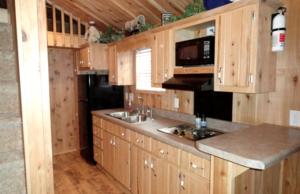 une cuisine avec des armoires en bois, un évier et un micro-ondes dans l'établissement Cozy Cabin Rental near the Custer State Park in South Dakota, à Sundance