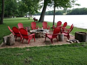 eine Gruppe roter Stühle um eine Feuerstelle am Wasser in der Unterkunft Rustic Waterfront Cottage Rental on the Guadalupe River in Texas in Schumannsville