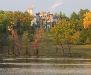 a large house sitting on top of a hill next to a lake at Spectacular Gothic-Style Castle with Private Pool and Hot Tub near Rindge, New Hampshire in Rindge