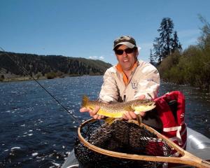 un homme dans un bateau tenant un poisson dans un panier dans l'établissement Fishing Getaway at a Riverside Resort near Beaverhead-Deerlodge National Forest, Montana, à Wise River