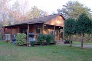 ein kleines Holzhaus mit einer Veranda auf einem Rasen in der Unterkunft Log Cabin Rental with Hot Tub near Hocking Hills State Park in Ohio in Cedar Grove