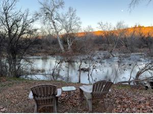 two chairs and a table in front of a river at Cozy Creekside Cottage with Deck and Fire Pit in Camp Verde, Arizona in Lake Montezuma