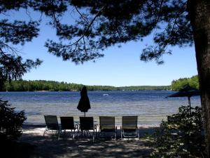 un tavolo con sedie e un ombrellone accanto a un lago di Cozy Cottage Rental with Lovely Beach Views on Halfmoon Lake, New Hampshire a New Durham