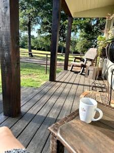 a wooden porch with a coffee cup on a table at Comfy Equipped Lodge Great for a Peaceful Getaway in Texas in Waelder +2 photos