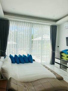 a large bed with blue pillows in front of a window at Baan Suan pool valley Villa in Ban Nong Thale