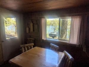 a dining room with a wooden table and two windows at Secluded Cabin Rental with Fireplace on Moose Lake near Eau Claire, Wisconsin in New Post +3 photos