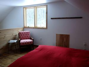 a bedroom with a red bed and a chair at Charming Cabin Getaway with a Wood-Burning Stove in Chesterfield, Massachusetts in South Worthington