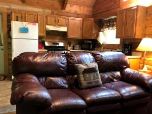 a brown leather couch in a kitchen with a white refrigerator at Charming Cabin Rental in the Forest near Beckley, West Virginia in Hico +15 photos