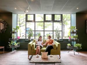 Dos mujeres sentadas en un sofá en una sala de estar en ibis Paris Bastille Opera, en París