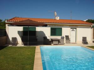 a swimming pool with an umbrella next to a house at Guest House dos Olivais in Azeitao