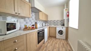 eine Küche mit Holzschränken, einer Waschmaschine und einem Trockner in der Unterkunft Sunrise Cottage in Llanddulas