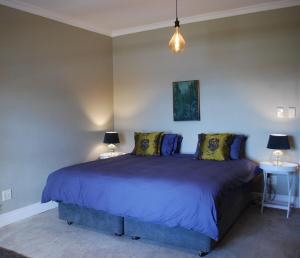 a bedroom with a bed with blue sheets and two lamps at Essio's Garden Apartment, Simons Town South Africa in Simonʼs Town
