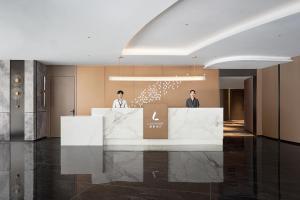 zwei Personen stehen an einem Tresen in einer Lobby in der Unterkunft Lavande Hotel Guangzhou Beijing Road Pedestrian Street Haizhu Square Metro Station Branch - Free Deliver Service to Canton Fair Complex During Canton Fair Period in Guangzhou