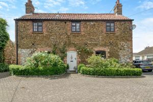 ein Backsteinhaus mit einer weißen Tür und einigen Büschen in der Unterkunft Carrstone Cottage in Grimston