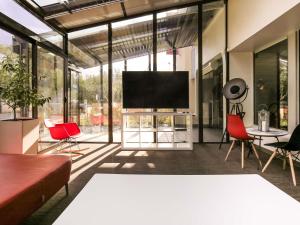 a living room with red chairs and a flat screen tv at ibis Paris Marne la Vallee Emerainville in Émerainville