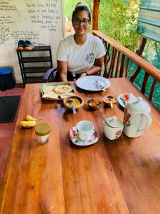 a woman sitting at a wooden table with food on it at Sigiri Village Vibe Hostel in Sigiriya