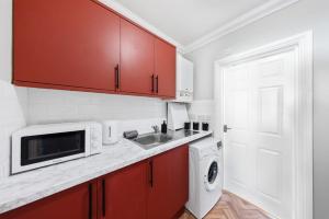 eine Küche mit roten Schränken und einer Spüle und einer Waschmaschine in der Unterkunft Long Stay Ready King Bed Kitchen WiFi Town in Gravesend