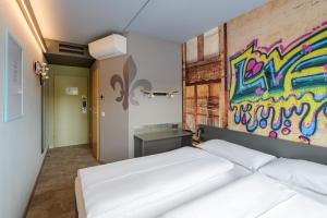 ダルムシュタットにあるFelix Hotel Darmstadtのベッドルーム1室(壁に落書きが施された白いベッド1台付)