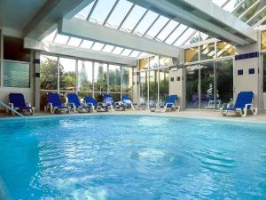 a swimming pool with blue chairs in a building at ibis Sète Balaruc les Bains Bien-être et Spa in Balaruc-les-Bains