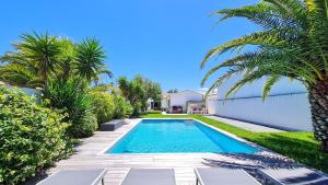 una piscina en un patio con palmeras en Superbe villa avec piscine chauffée, boulodrome et parking, en Sainte-Marie-de-Ré