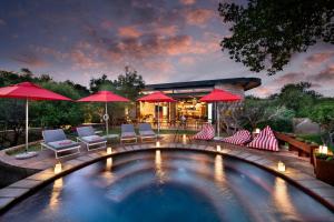 a swimming pool with chairs and umbrellas in a backyard at Mbazo Safari Collection in Pilanesberg