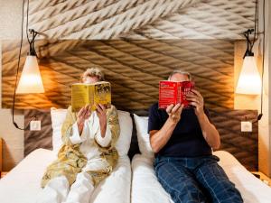 a man and a woman sitting in bed reading books at Ibis Paris Gare Montparnasse 15ème in Paris