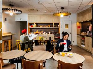 a woman sitting at tables in a restaurant looking at her cell phone at Ibis Paris Gare Montparnasse 15ème in Paris