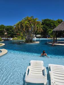 a man swimming in a swimming pool with two chairs at Iloa resort AP luxo in Barra de São Miguel