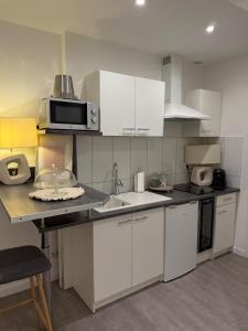 Una cocina con gabinetes blancos, un fregadero y un microondas. en Spa sauna et hammam - Dahlia, en Belfort