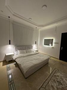 a white bedroom with a large bed and two tables at شقه غرفه وصاله هادئه in Buraydah +11 photos