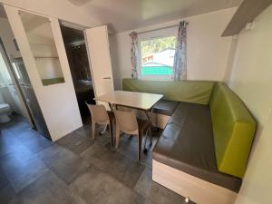 a dining room with a table and a green couch at Escale Nature - Bungalow F14 pour 4 au camping Le Ried in Boofzheim