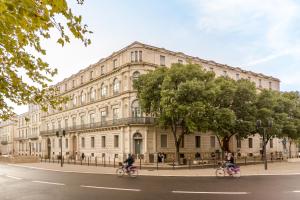 two people riding bikes in front of a large building at Appart'City Collection Nîmes Arènes in Nîmes