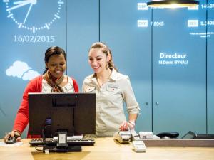 zwei Frauen stehen hinter einem Schreibtisch mit einem Computer in der Unterkunft Hotel ibis Lisboa Saldanha in Lissabon