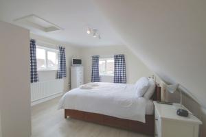 a white bedroom with a bed and two windows at Tofts, East Wittering in East Wittering