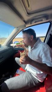 een man die in een auto zit en een broodje eet bij Köşk Rezidans 