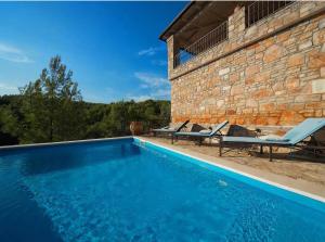 a swimming pool in front of a stone building with two chairs at Villa Rosa in Vrboska