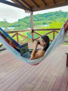 a woman laying in a hammock taking a picture of a laptop at Casa da Sorte - campo, montanha, natureza e caminho da praia in Santo Amaro da Imperatriz